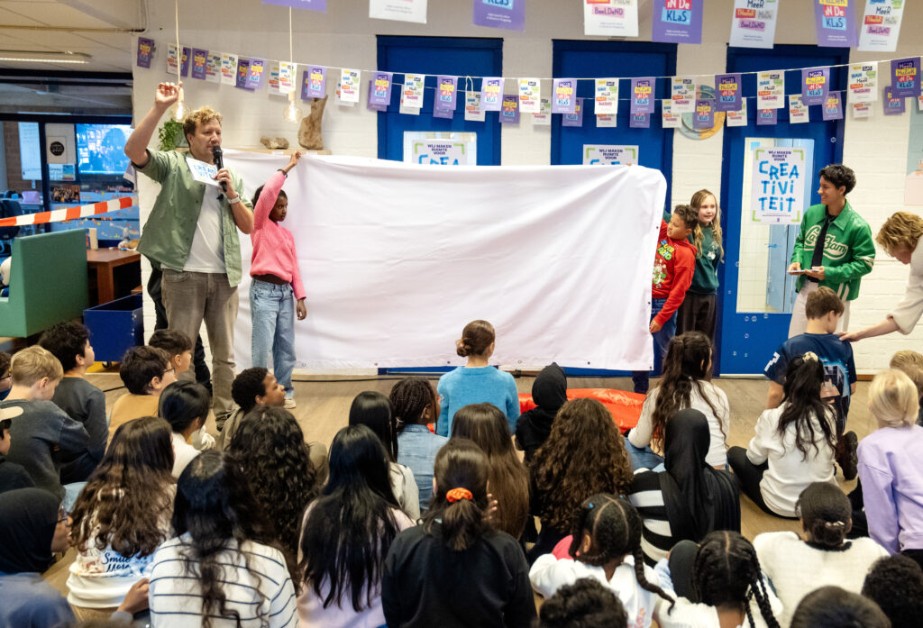 Het creatieve doek, een groot wit doek van 3 meter breed en 1,5 meter hoog, wordt onthuld door Klaas van Kruistum en enkele leerlingen.